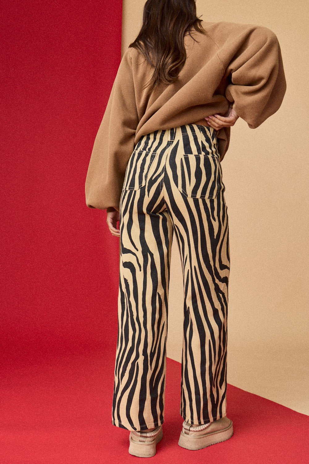 Person wearing zebra print pants and a beige sweater on a red and beige background