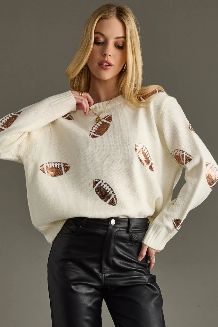 Woman wearing a white sweater with sequin football on a gray background