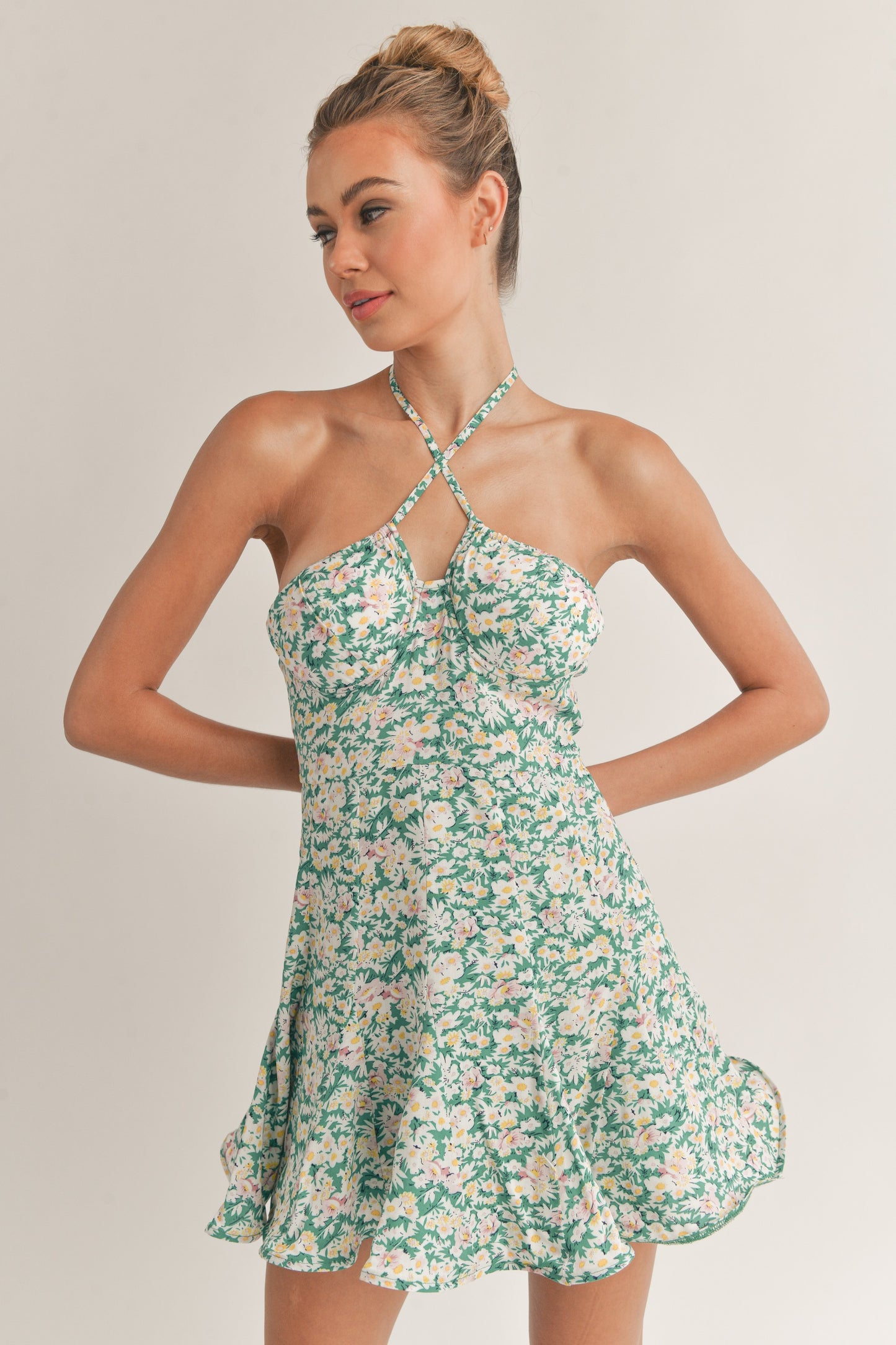 Woman wearing a green floral halter mini dress with a fitted bodice and flared skirt.
