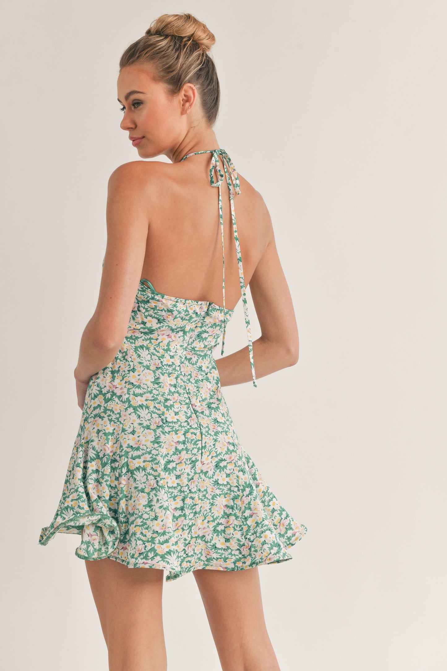 Woman wearing a green floral halter mini dress with a fitted bodice and flared skirt.
