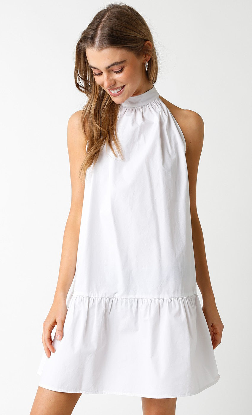 Woman wearing a sleeveless white halter mini dress with a high neckline and a bow-tie back detail.