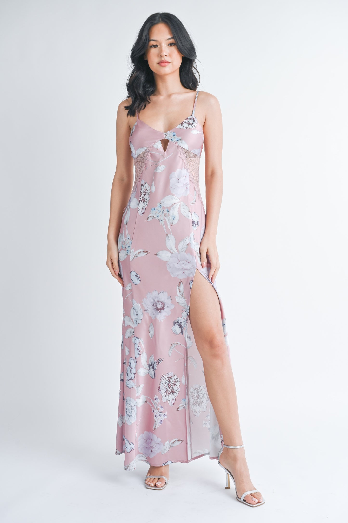 Woman wearing a long mauve floral slip dress with a front slit and lace side panels.