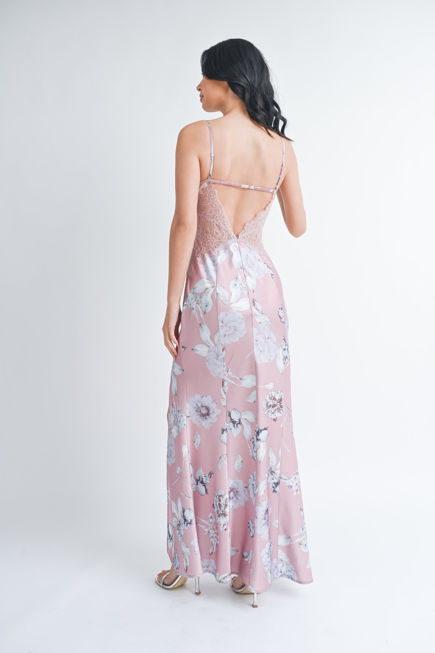 Woman wearing a long mauve floral slip dress with a front slit and lace side panels.