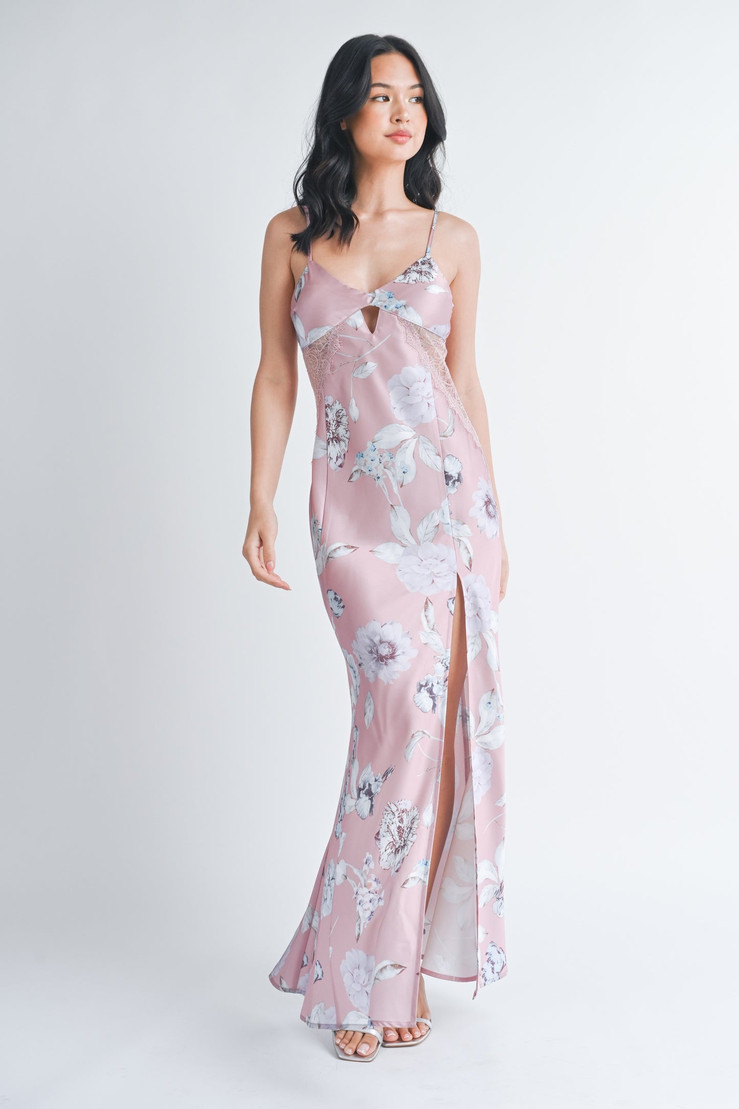 Woman wearing a long mauve floral slip dress with a front slit and lace side panels.