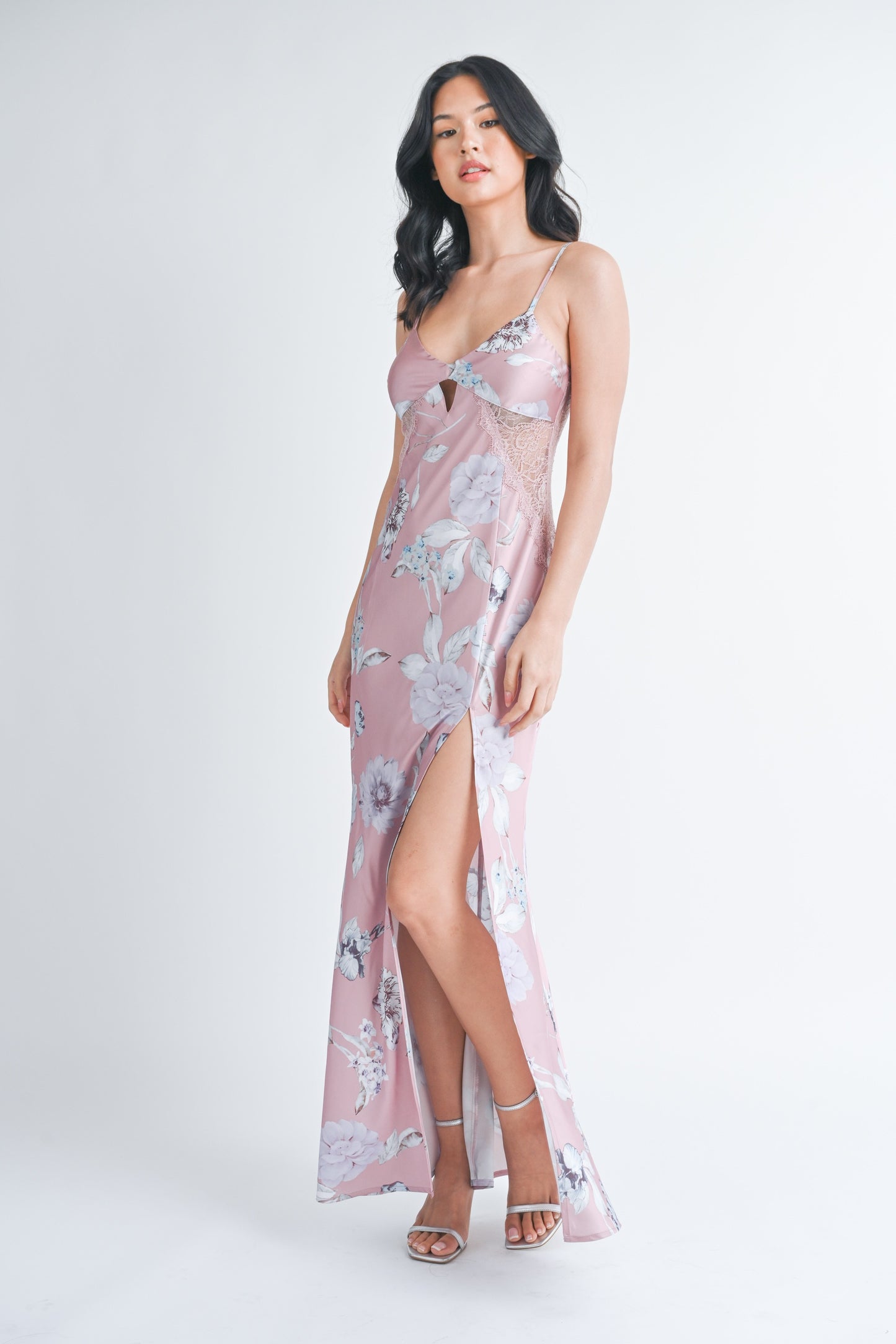 Woman wearing a long mauve floral slip dress with a front slit and lace side panels.