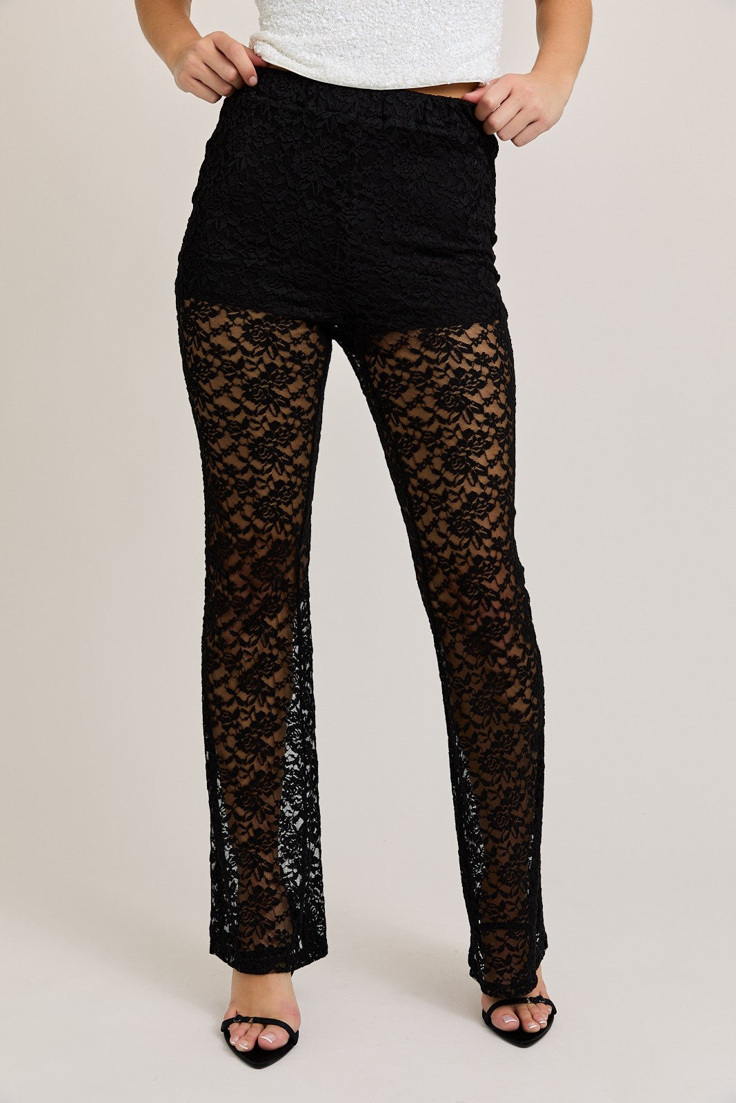 Woman wearing black high-waisted lace flare pants with a partially lined design and sheer leg detailing, styled with black heels for a chic and edgy look.