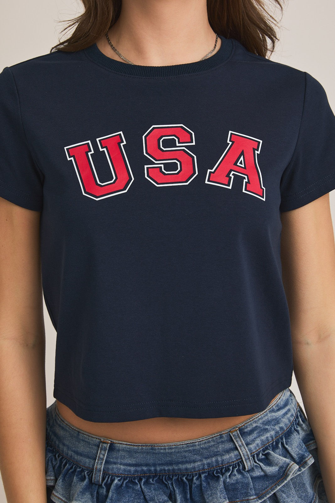 Close-up of a navy blue cropped t-shirt with bold red “USA” lettering outlined in white across the chest.