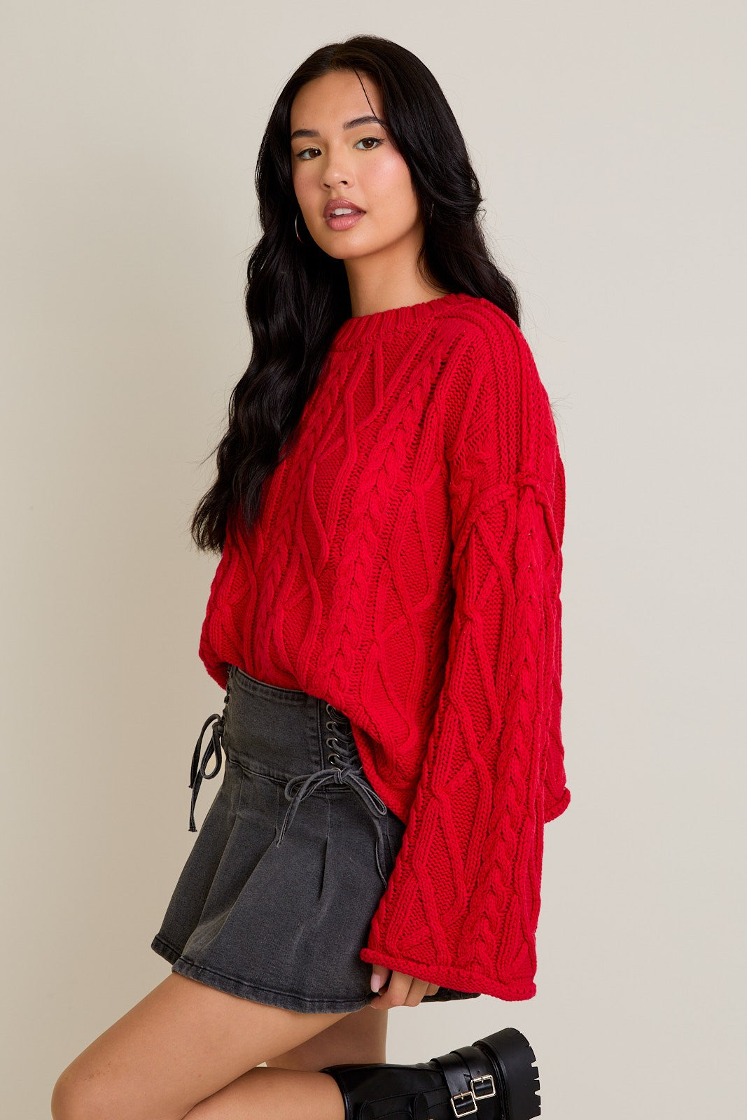 Woman wearing a red cable knit sweater and black skirt on a beige background