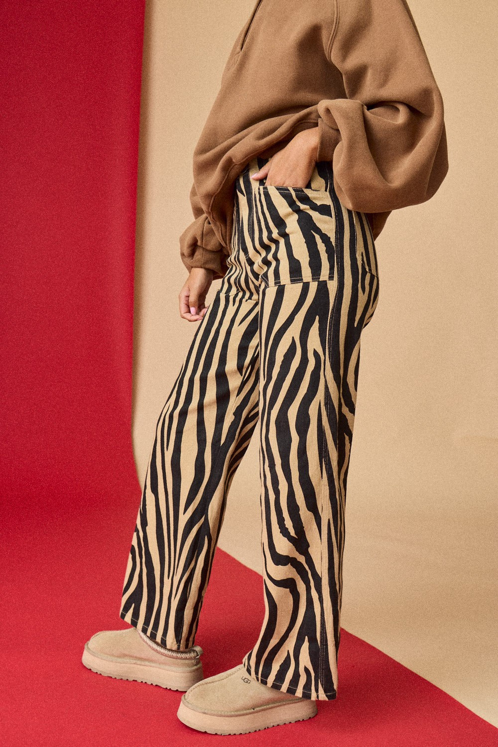 Person wearing zebra print pants and a brown sweater on a red and beige background