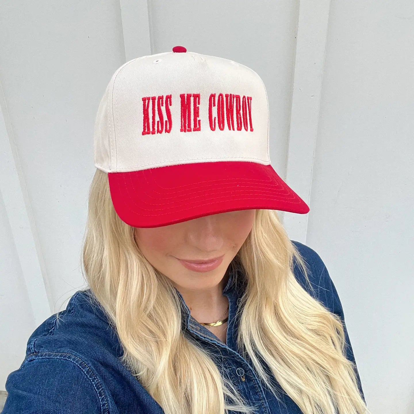 Beige and red trucker hat with bold red embroidered text that says "Kiss Me Cowboy, worn on a models head