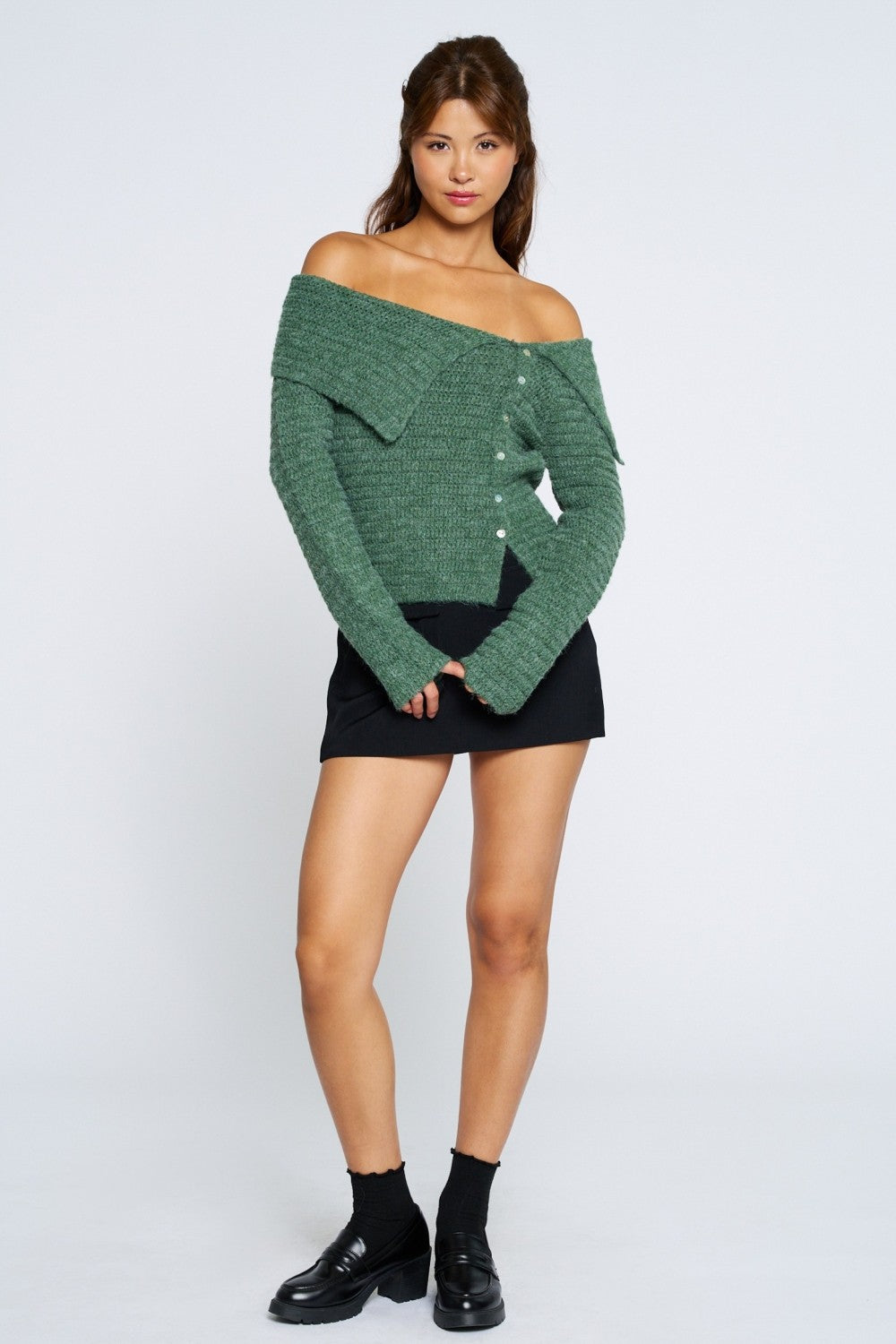 Woman wearing a green off-shoulder sweater and black skirt on a white background