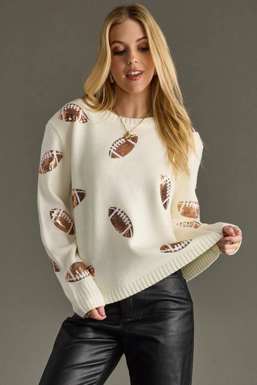 Woman wearing a cream sweater with sequin football patterns against a gray background