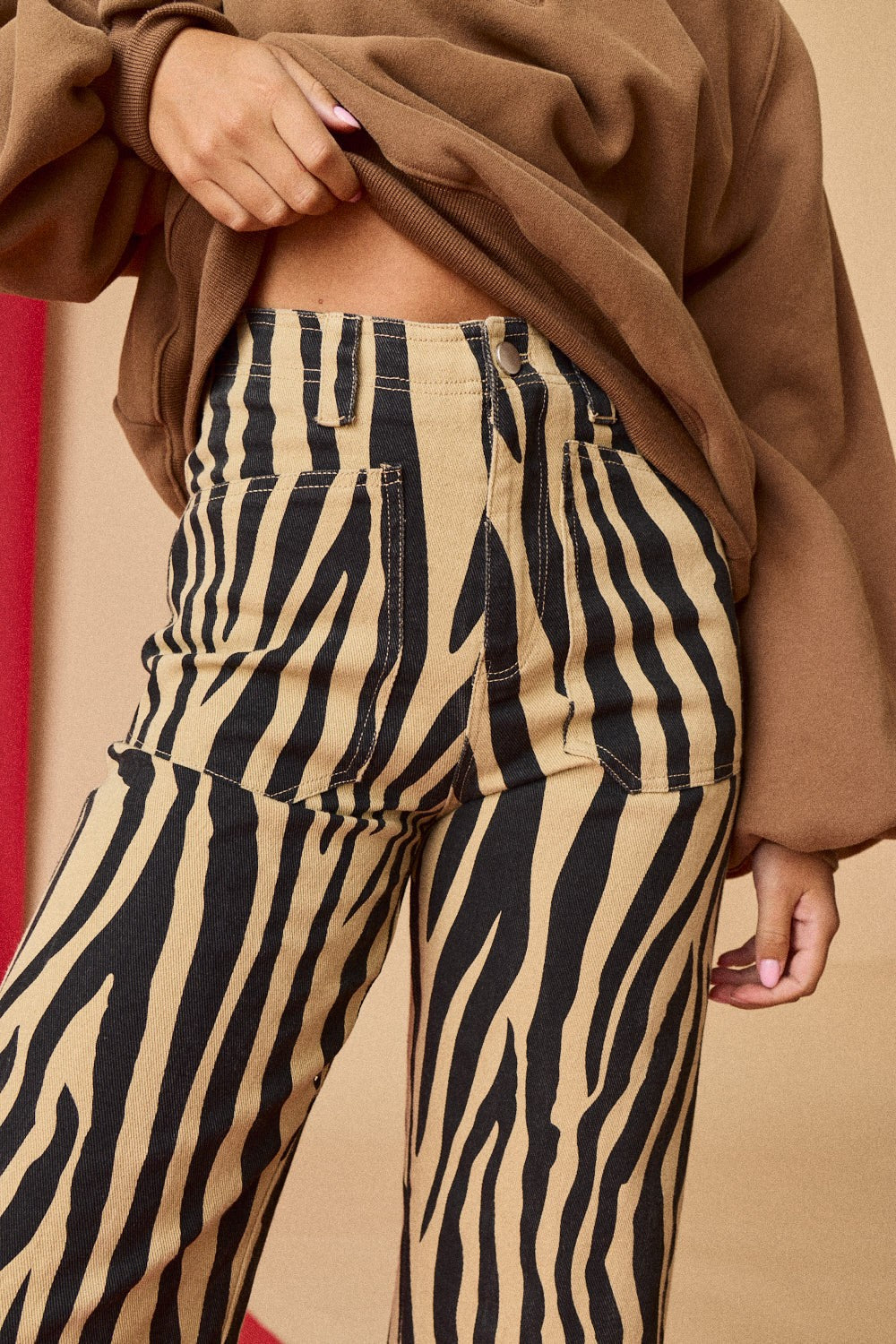Person wearing zebra print pants with a brown coat against a beige background