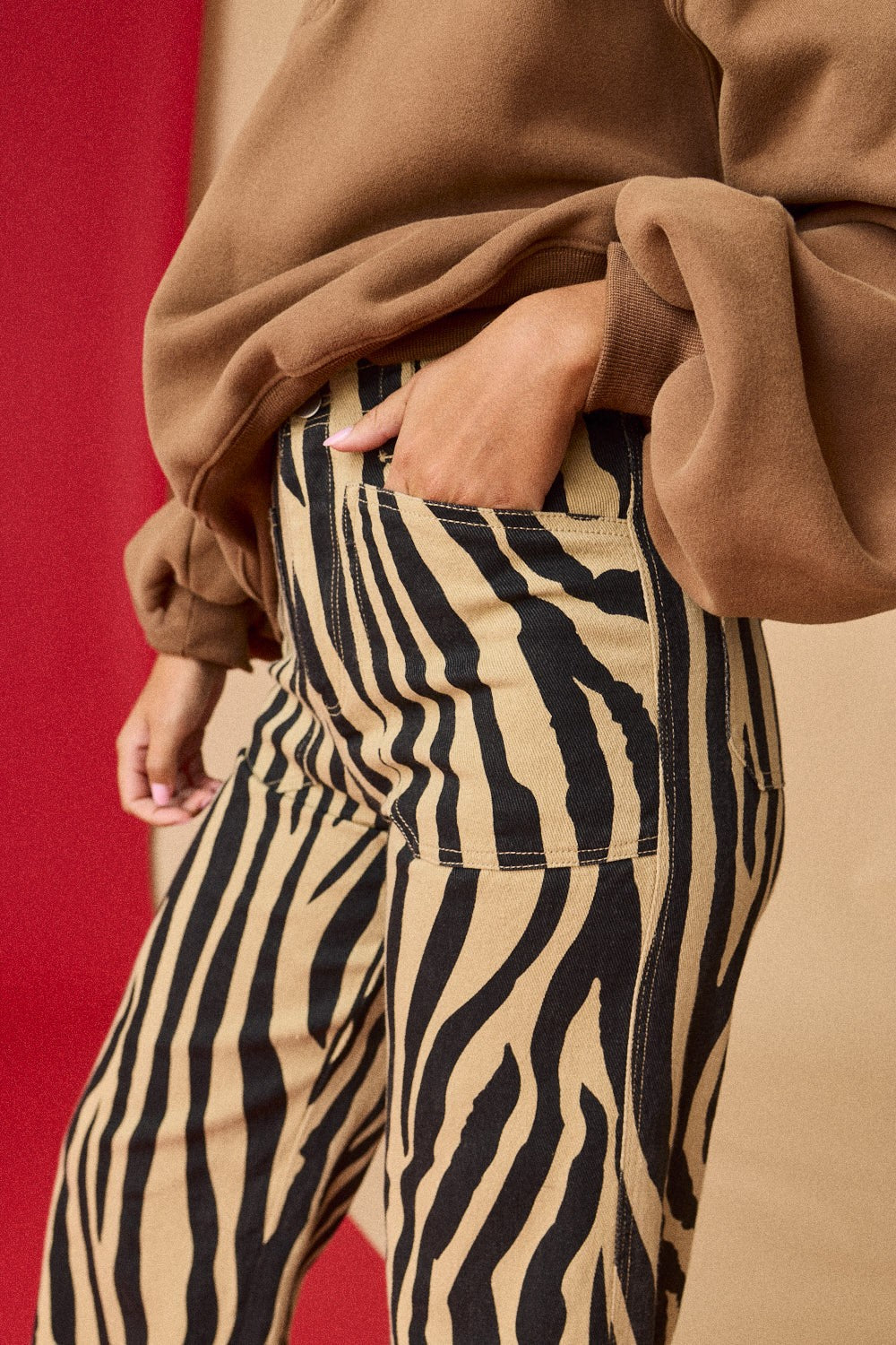 Person wearing a brown coat and zebra-striped pants against a red background