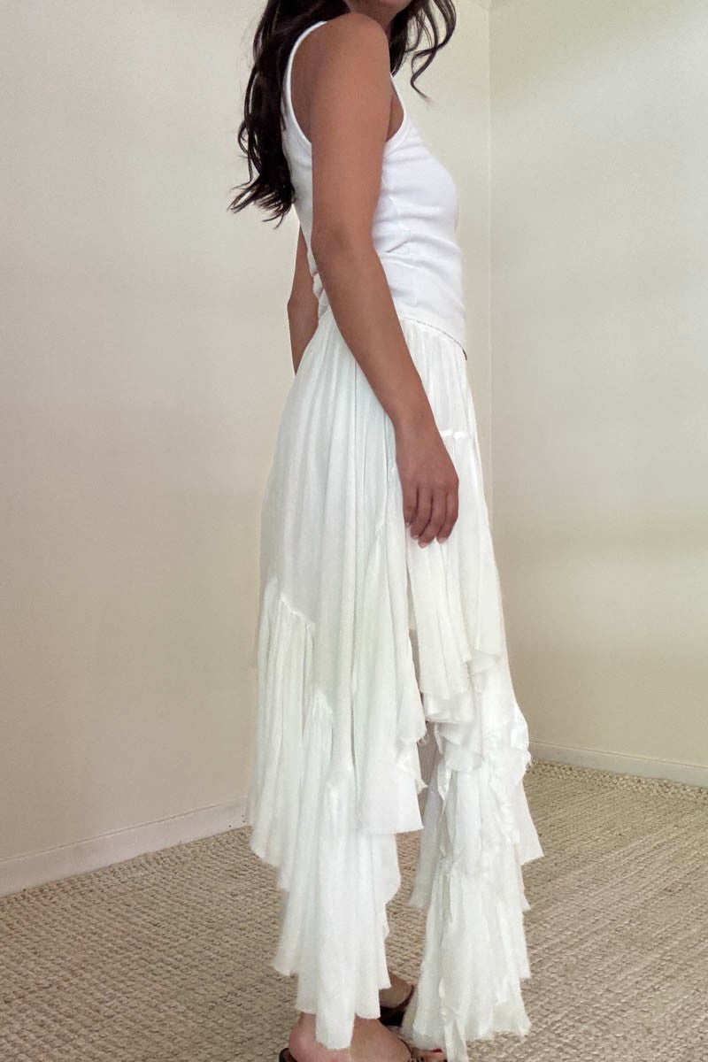 Side view of a woman wearing a white tank top and a cascading white tiered skirt, showing the layered detail and soft flow of the fabric.