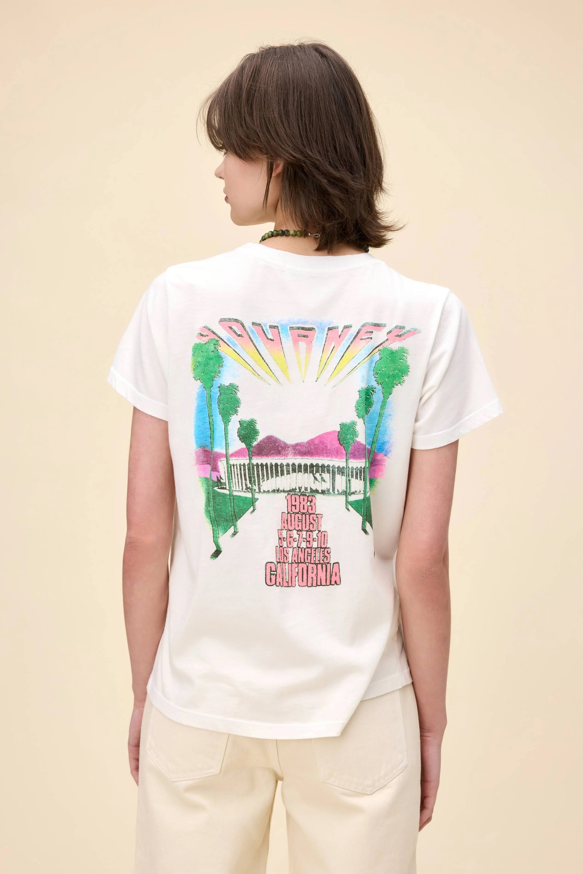 Vintage-inspired Journey California Rock & Roll graphic tee, featuring a bold retro helmet design on the front with colorful gradient lettering. The back showcases a 1983 Los Angeles concert graphic with palm trees and a sunset aesthetic. Designed in a relaxed fit, this lightweight tee is perfect for music lovers and casual streetwear.