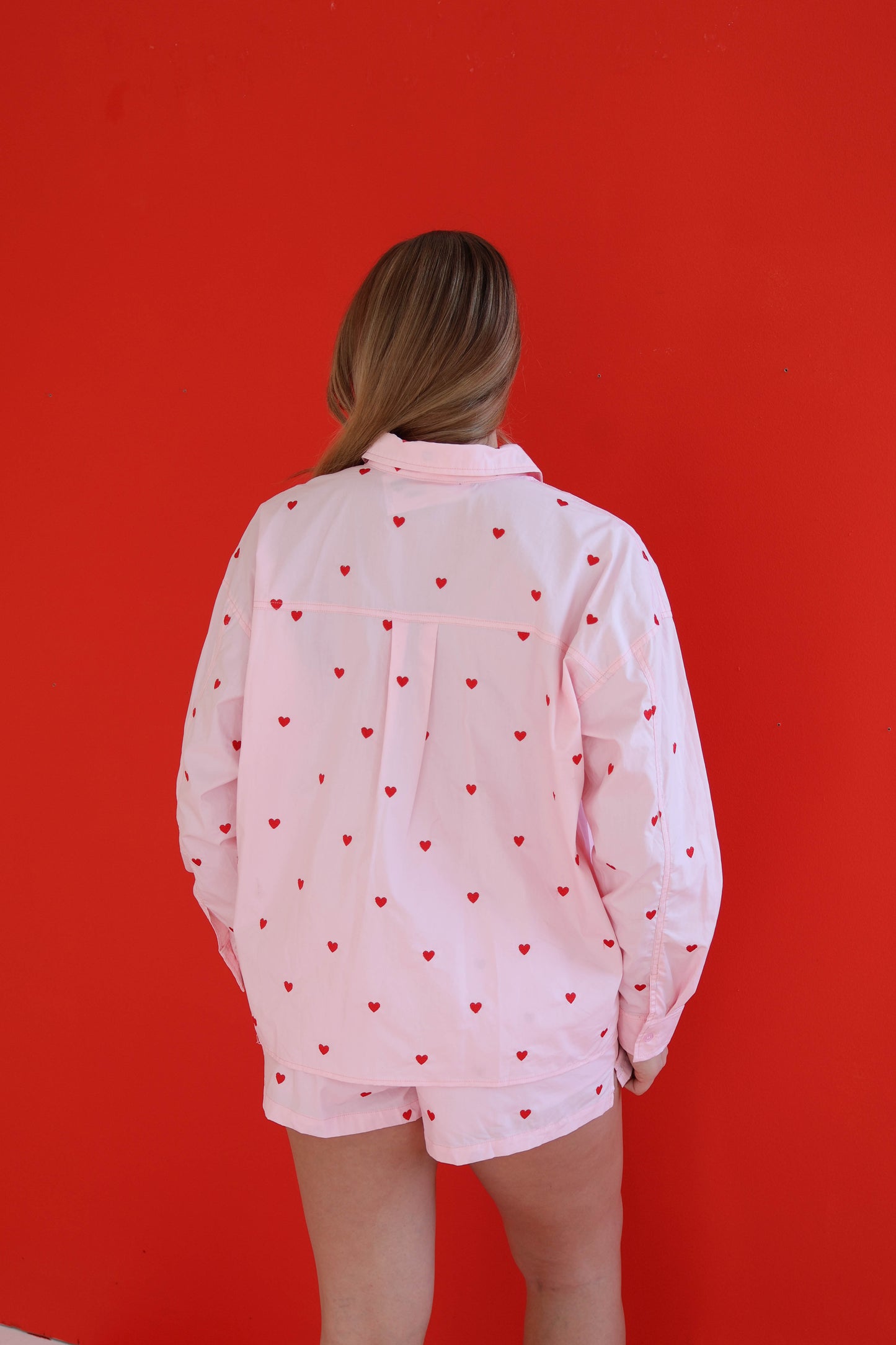 Person wearing a light pink outfit with red heart patterns against a red background