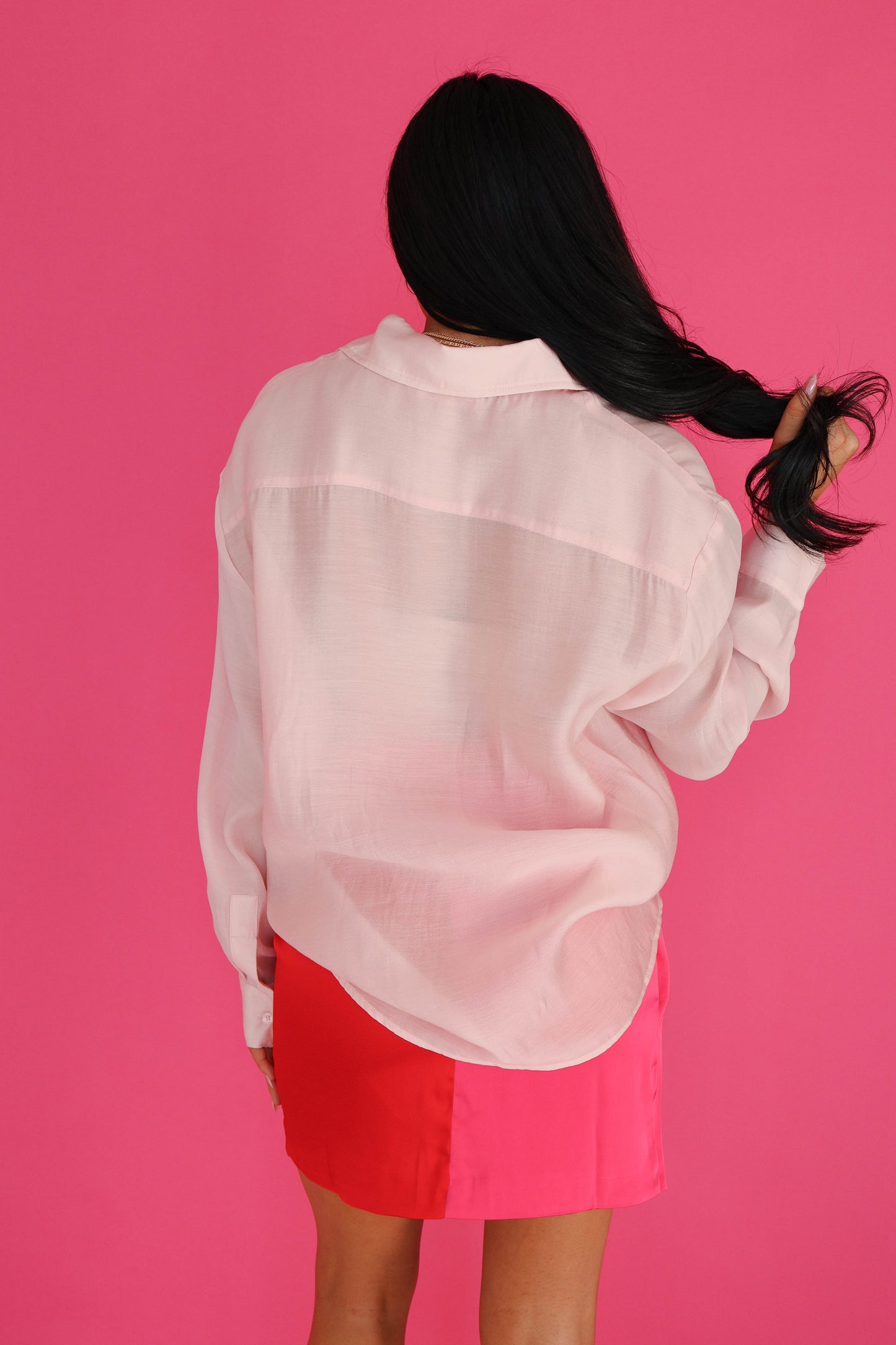 Person wearing a light pink sheer blouse and red shorts against a pink background