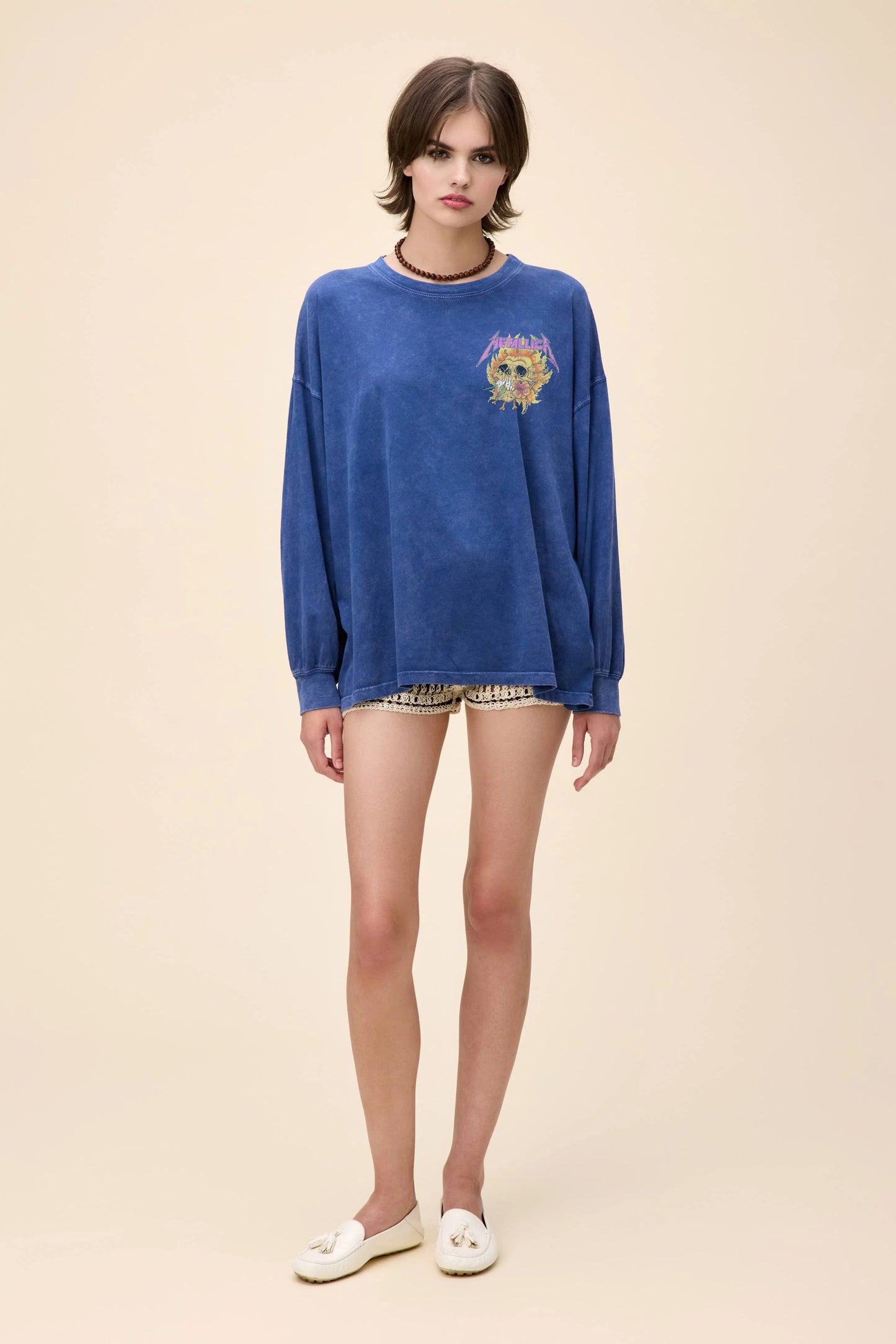 Front and back view of a blue oversized long sleeve Metallica graphic tee featuring a flaming flower skull design on the front and back, worn with crochet shorts.