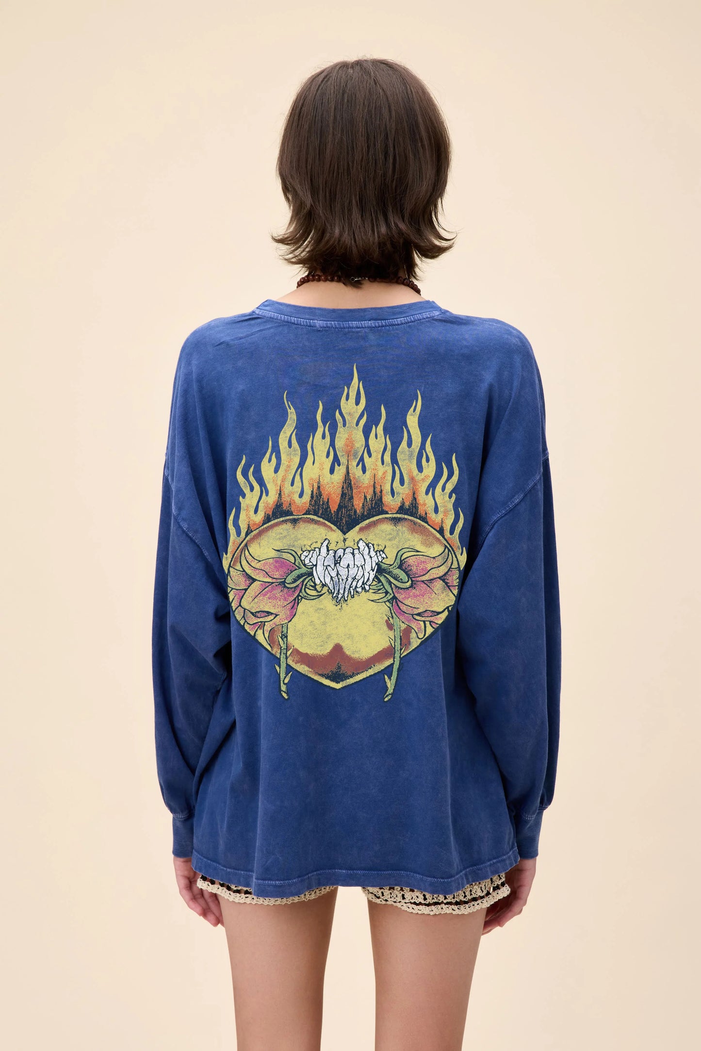 back view of a blue oversized long sleeve Metallica graphic tee featuring a flaming flower skull design on the front and back, worn with crochet shorts.