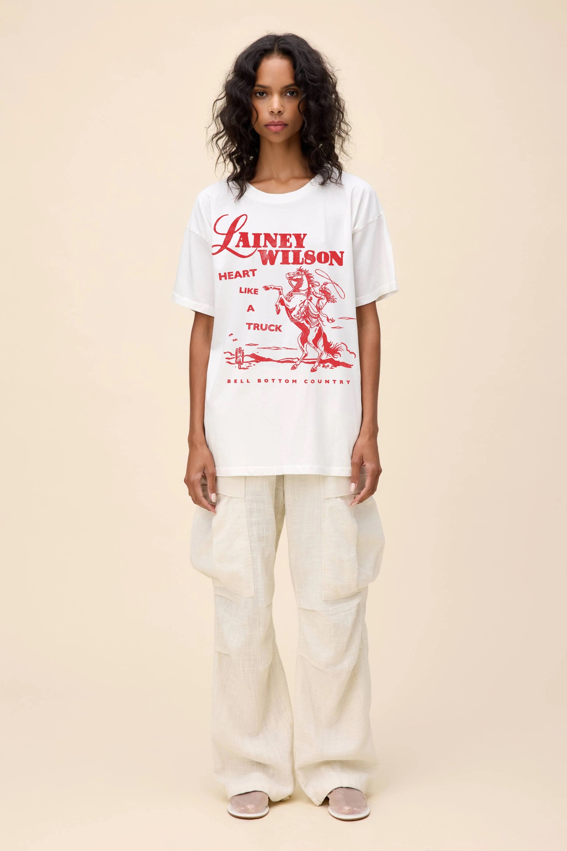 White oversized graphic tee featuring Lainey Wilson’s "Heart Like a Truck" design in bold red lettering with a vintage Western-style illustration of a cowboy on horseback.