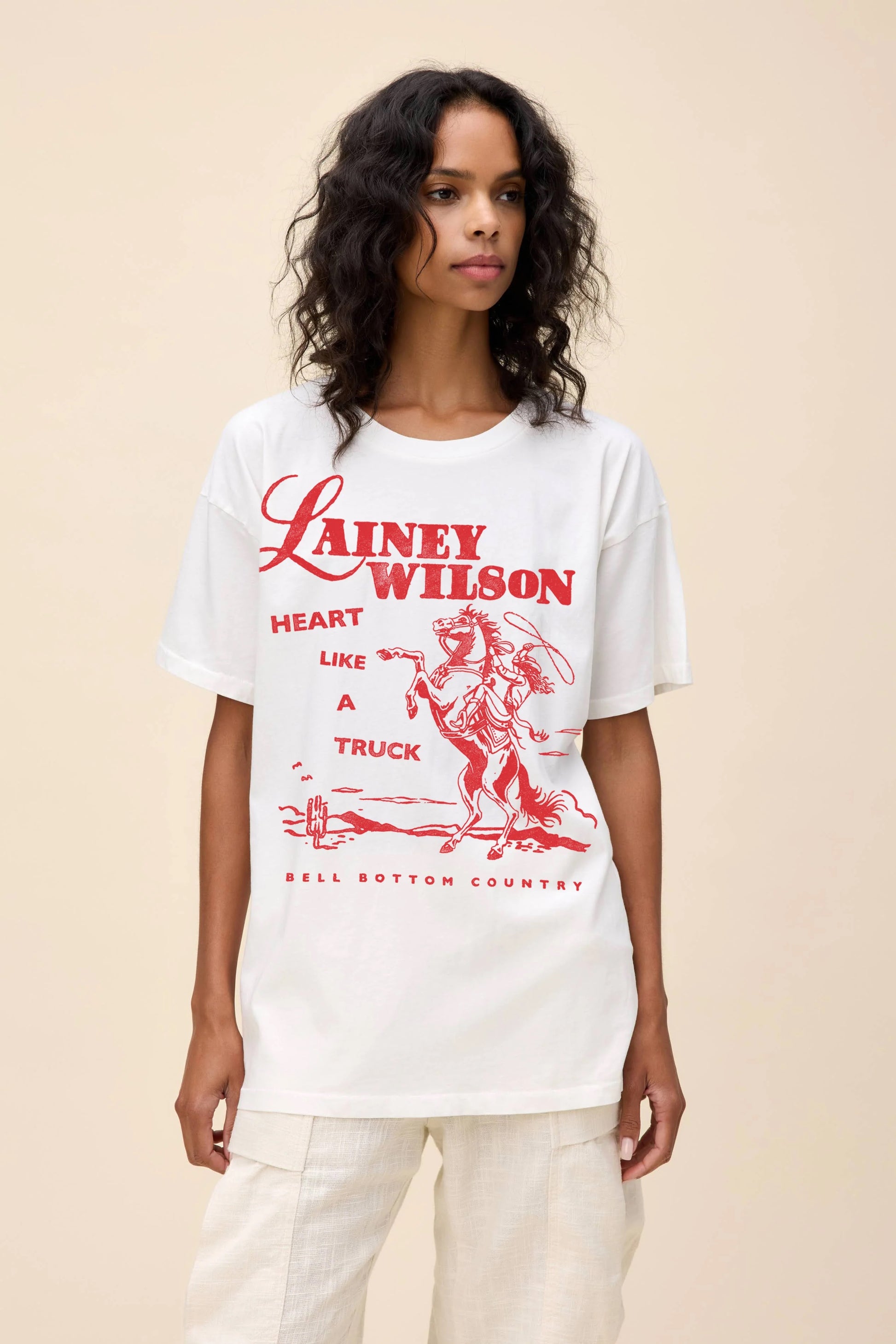 White oversized graphic tee featuring Lainey Wilson’s "Heart Like a Truck" design in bold red lettering with a vintage Western-style illustration of a cowboy on horseback.