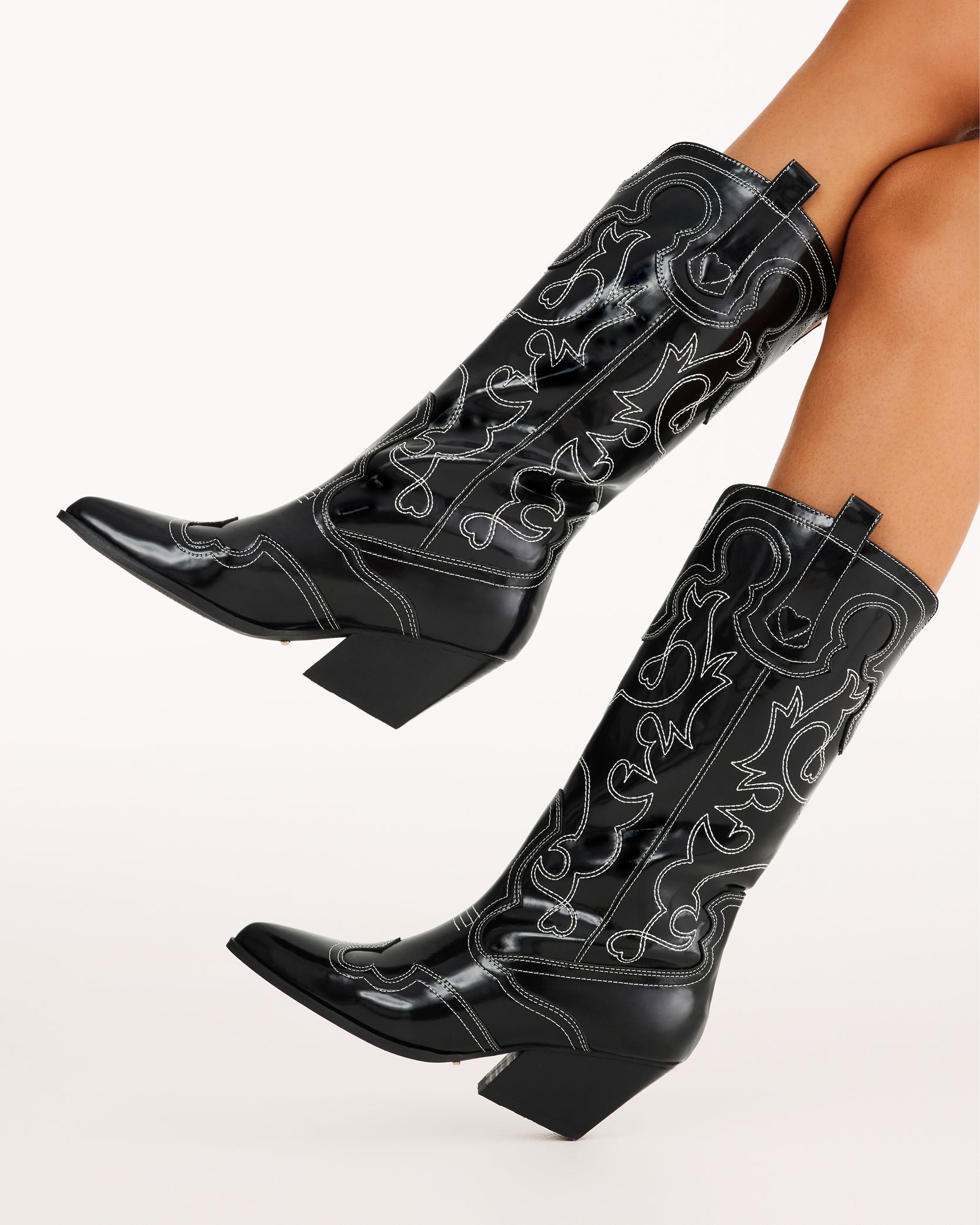 Sleek and bold, these black patent western boots feature contrasting white stitching, a pointed toe, and a stacked angled heel for a modern twist on classic cowboy style. Perfect for concerts, festivals, and statement outfits.