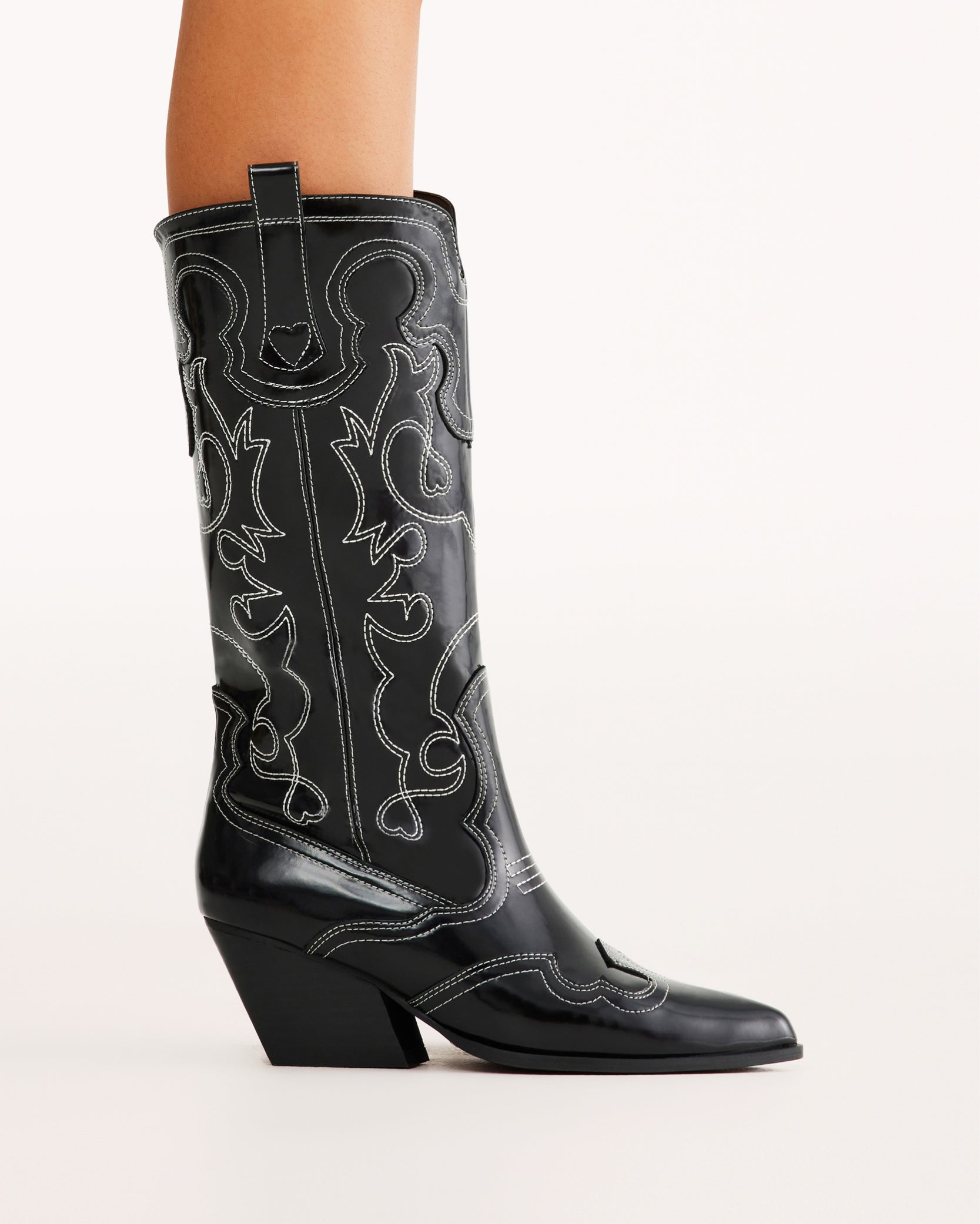 Sleek and bold, these black patent western boots feature contrasting white stitching, a pointed toe, and a stacked angled heel for a modern twist on classic cowboy style. Perfect for concerts, festivals, and statement outfits.