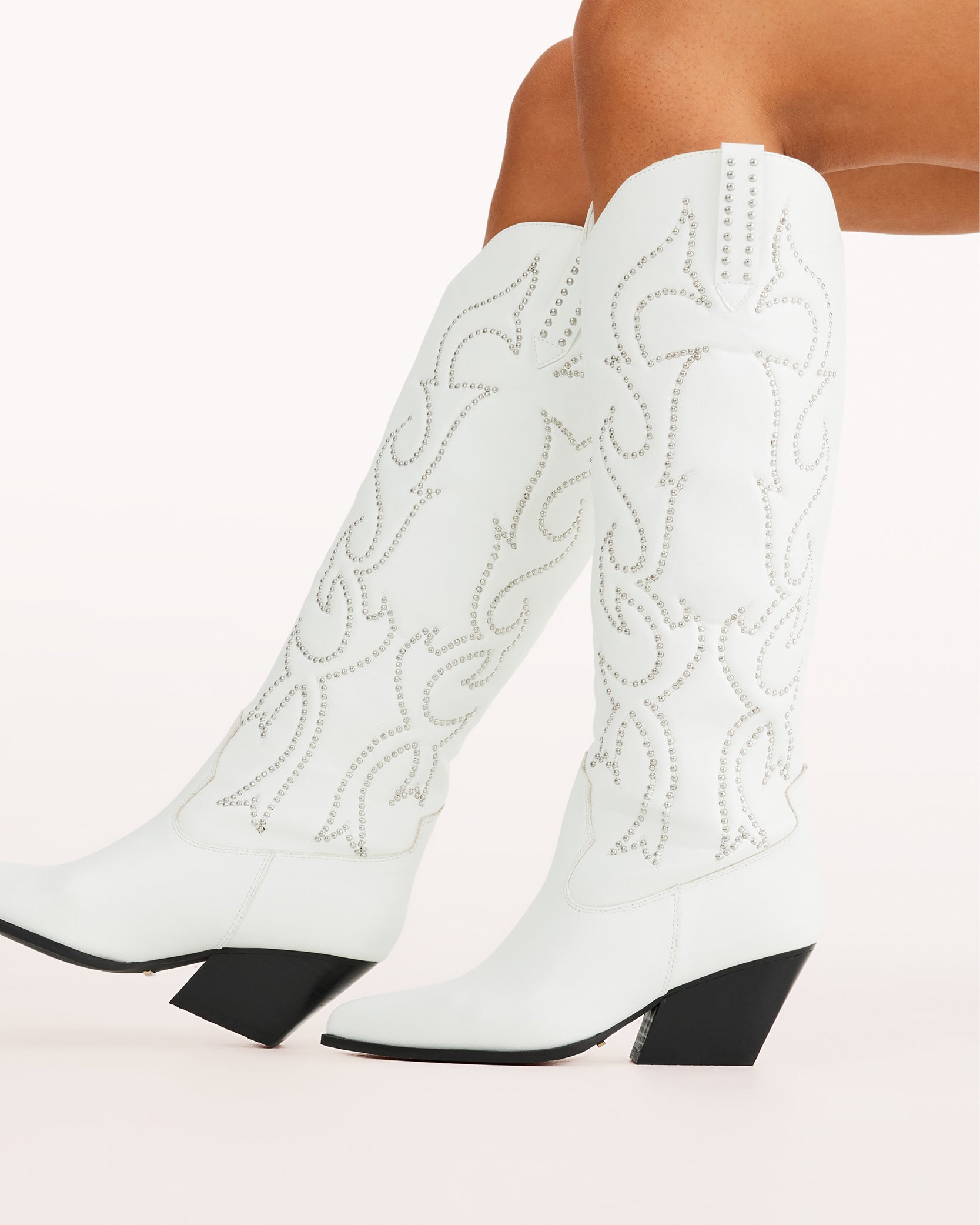 Chic and bold, these white western knee-high boots feature classic cowboy stitching with silver stud embellishments, a pointed toe, and a stacked angled heel. Perfect for country concerts, bachelorette parties, festivals, or trendy street style looks.