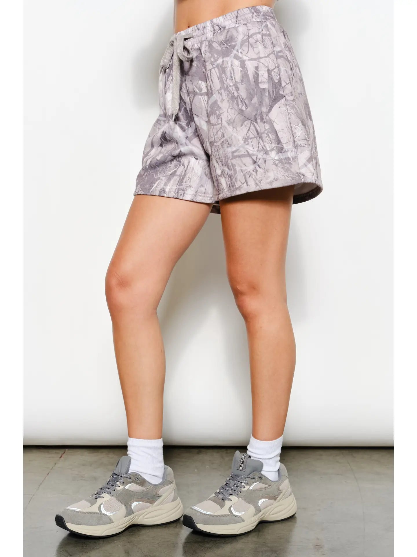 Person wearing gray patterned shorts and sneakers on a white background