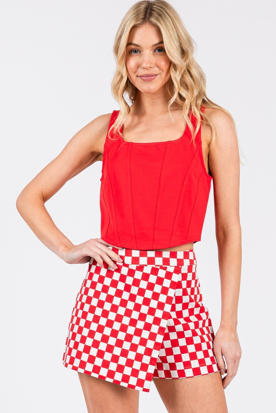 Woman wearing a red sleeveless top and red and white checkered shorts on a light gray background