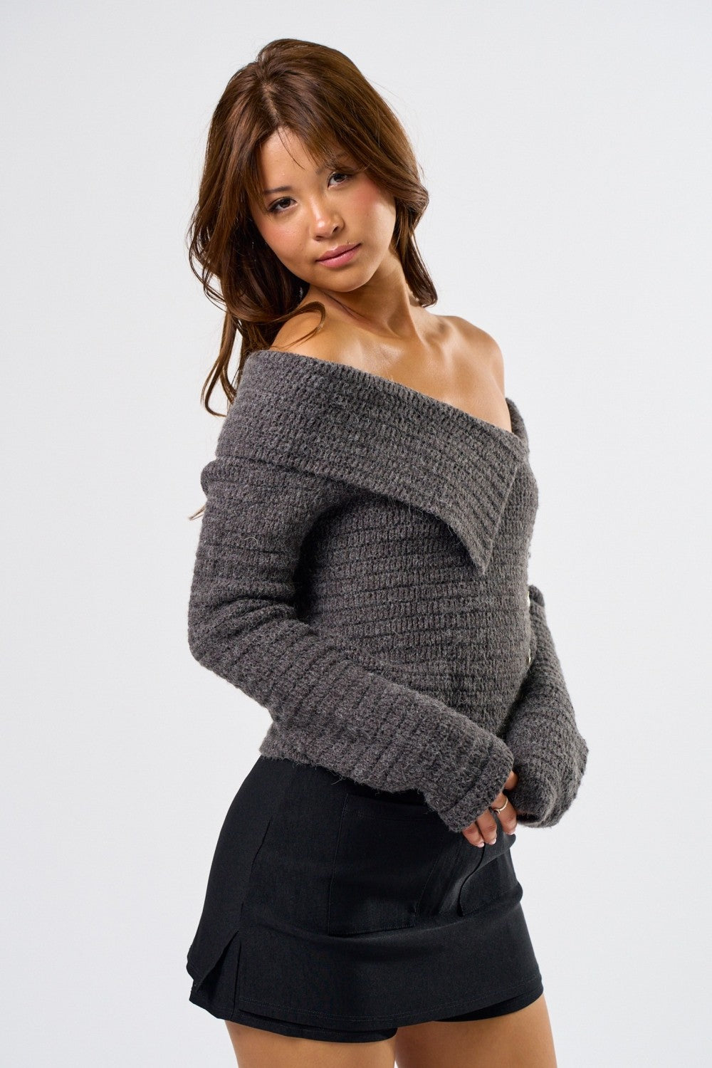 Woman wearing a gray off-shoulder sweater and black skirt on a white background