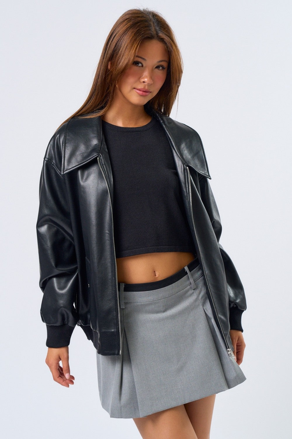 Woman wearing a black leather jacket, black top, and gray skirt on a white background