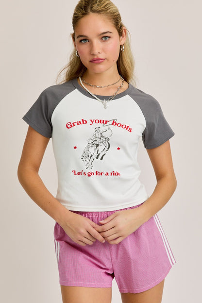 Model wearing a western-style graphic baby tee with grey sleeves and red cowboy text that reads “Grab your boots, let’s go for a ride”