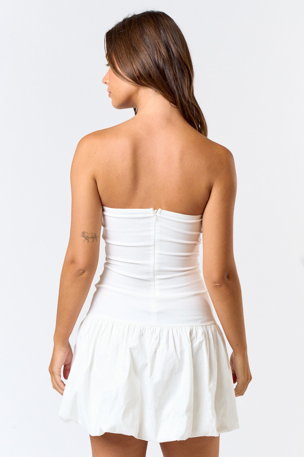 back of Woman wearing a strapless white mini dress with a deep V-notch neckline and a bubble hem skirt, posing against a plain white background.
