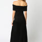 back view Woman wearing a black off-the-shoulder maxi dress with a fitted bodice and pleated floor-length skirt, standing against a white background.
