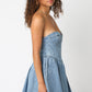Side view of a woman wearing a strapless denim mini dress with a flared skirt and corset-style bodice.