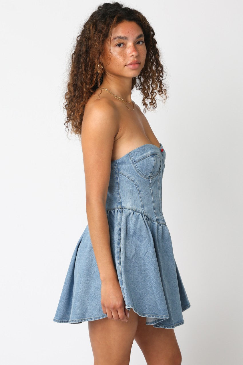 Side view of a woman wearing a strapless denim mini dress with a flared skirt and corset-style bodice.