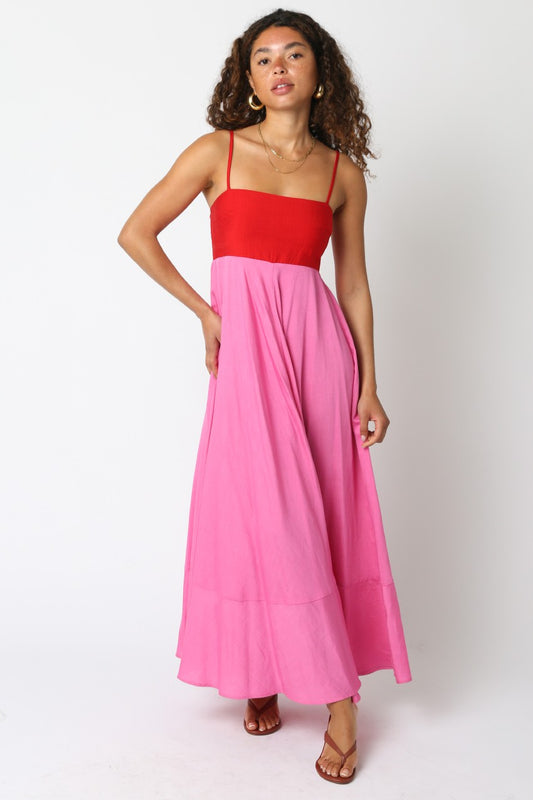Woman wearing a red and pink colorblock maxi dress with spaghetti straps and a flowing skirt, standing against a plain white background.