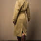 Woman wearing a long beige trench coat and brown boots against a plain background