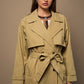 Woman wearing a beige trench coat against a brown background