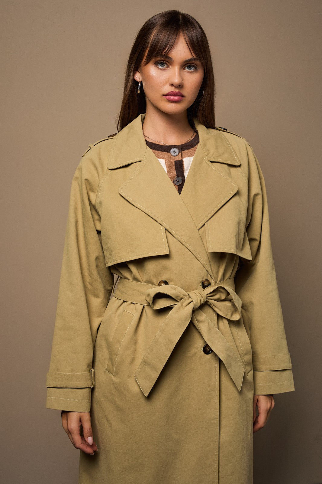 Woman wearing a beige trench coat against a brown background