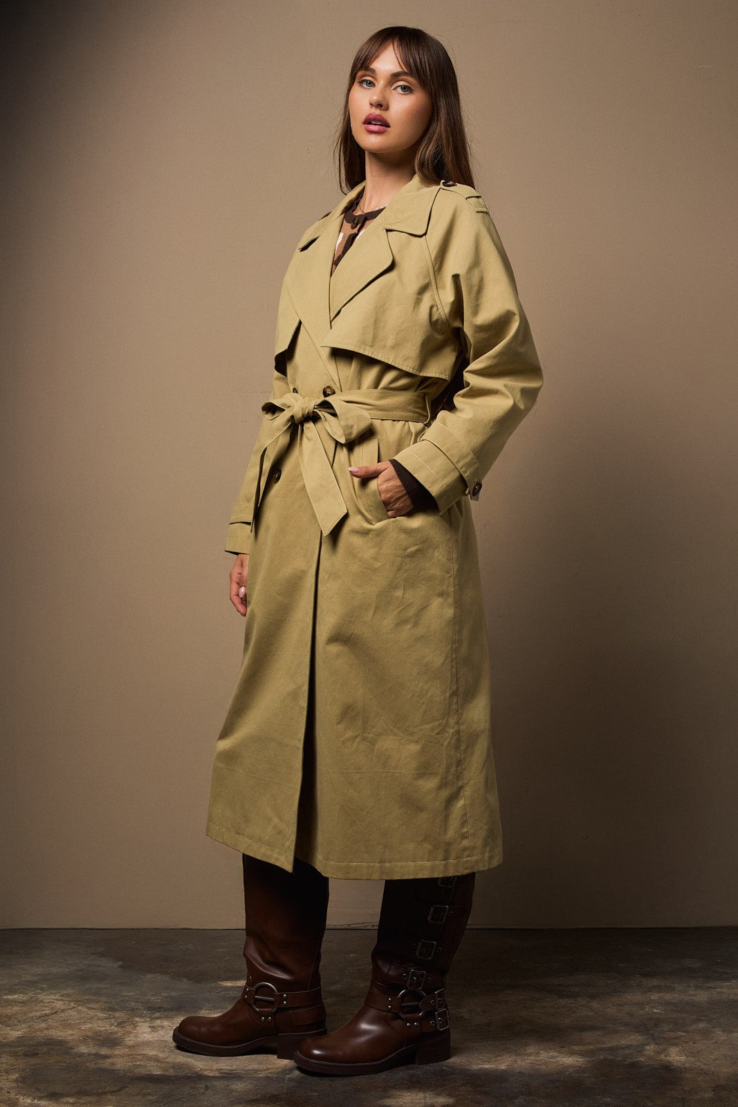 Woman wearing a light green trench coat against a plain background