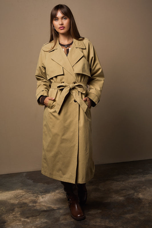 Woman wearing a beige trench coat against a plain background