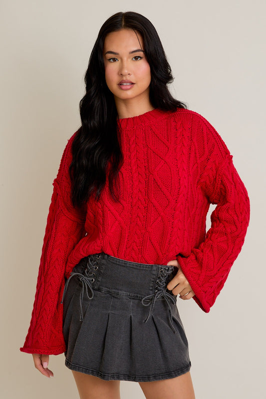 Woman wearing a red cable knit sweater and black skirt against a neutral background