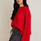 Woman wearing a red cable knit sweater and black skirt on a beige background