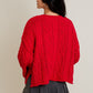 Person wearing a red cable knit sweater and dark gray skirt on a beige background