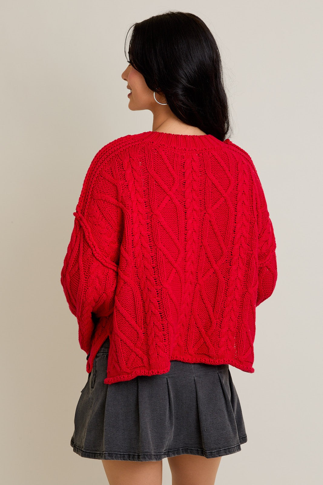 Person wearing a red cable knit sweater and dark gray skirt on a beige background