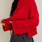 Person wearing a red cable knit sweater and black skirt against a plain background