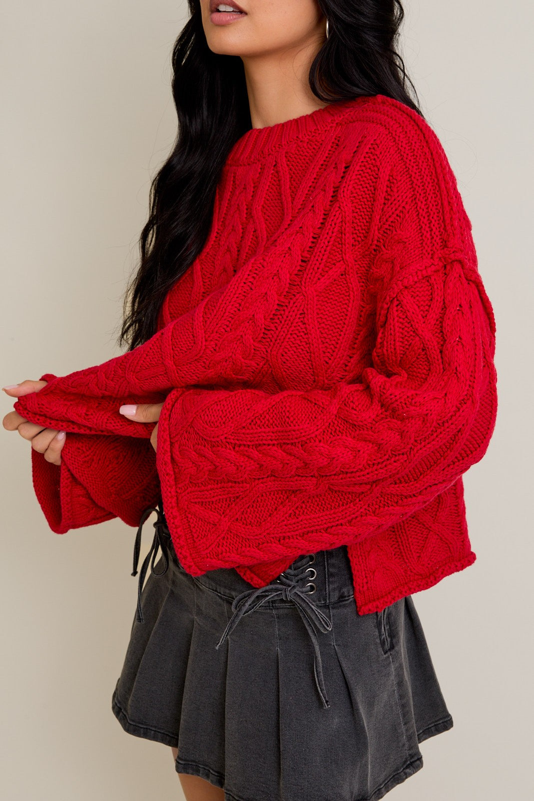 Person wearing a red cable knit sweater and black skirt against a plain background